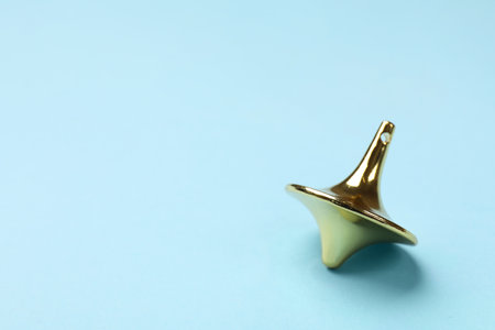 One golden spinning top on light blue background, closeup. Space for textの写真素材