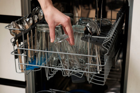Woman loading dishwasher with glass and cutlery indoors, closeupの写真素材