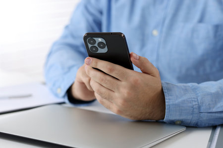 Man using smartphone at table in office, closeup