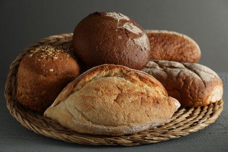 Wicker basket with different types of fresh bread on gray wooden table, closeup