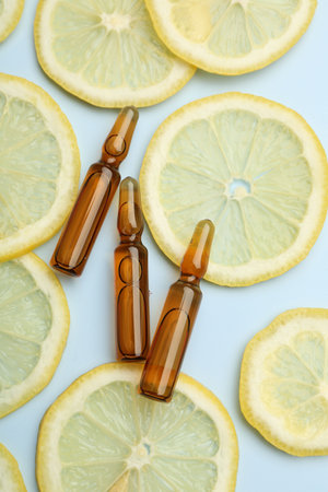 Skincare ampoules with vitamin C and slices of lemon on light blue background, flat layの写真素材