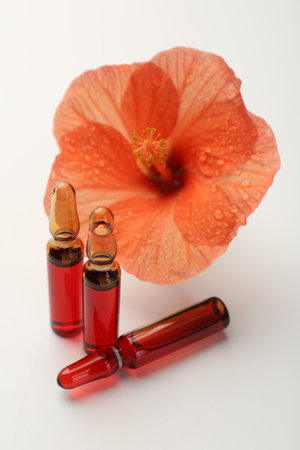 Skincare ampoules and hibiscus flower on white backgroundの写真素材