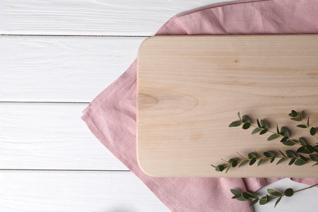 Cutting board, green branch and napkin on white wooden table, top view. Space for textの写真素材