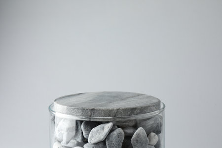 Presentation for product. Glass container with stones on light gray background. Space for text