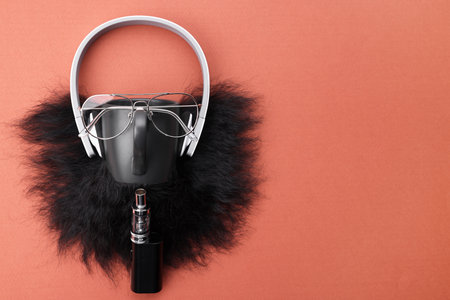 Man's face made of artificial beard, headphones and glasses on terracotta background, top view....