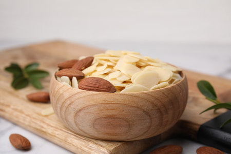 Fresh almond flakes and nuts in bowl on white table, closeupの写真素材