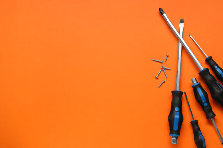 Set of screwdrivers and screws on orange background, flat lay. Space for textの写真素材