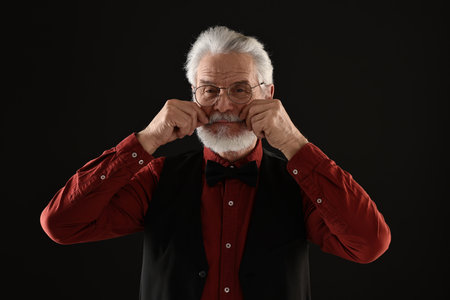 Senior man touching mustache on black backgroundの写真素材