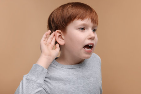 Little boy with hearing problem on pale brown backgroundの写真素材