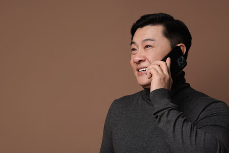 Portrait of happy man with smartphone on brown background. Space for text