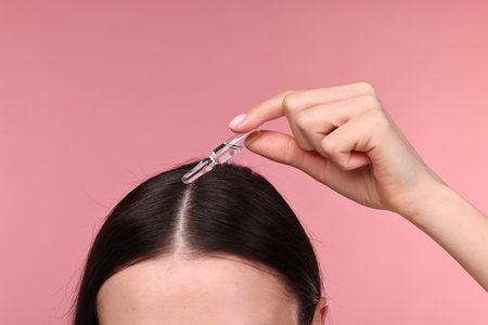 Beautiful young woman using ampoule for hair treatment on pink background, closeupの写真素材