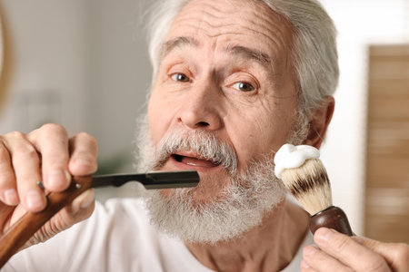 Man shaving mustache and beard with blade in bathroomの写真素材