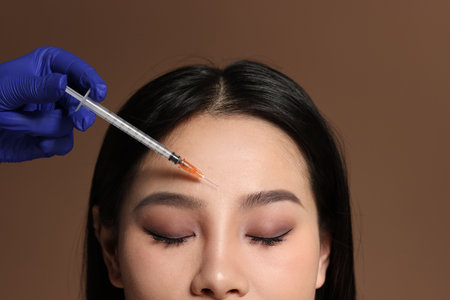 Woman getting facial injection on brown background, closeupの写真素材