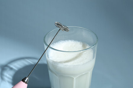 Mini mixer (milk frother) and whipped milk in glass on light blue background, closeupの写真素材