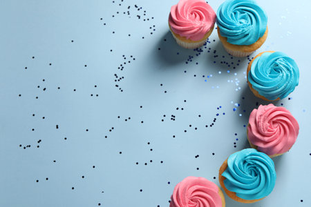 Delicious cupcakes with bright cream and confetti on light blue background, flat lay. Space for textの写真素材