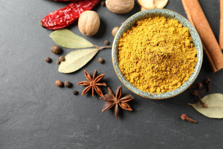 Dry curry powder in bowl and other spices on dark textured table, flat lay. Space for textの写真素材