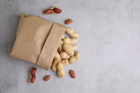 Paper bag with fresh unpeeled peanuts on gray table, top view. Space for text