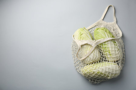 Fresh Chinese cabbages in string bag on light background, top view. Space for textの写真素材