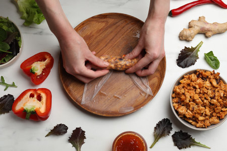 Woman making tasty spring roll at white marble table, top view