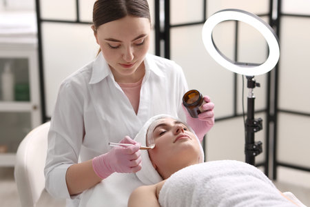 Cosmetologist applying mask on woman's face in clinicの写真素材