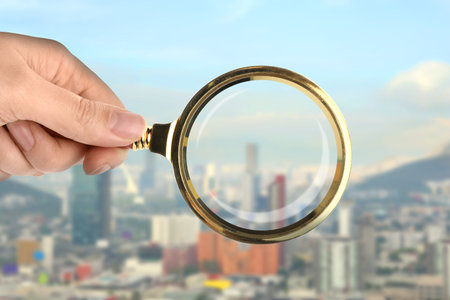 Woman holding magnifying glass against city, closeup. Search for apartmentの写真素材