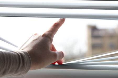 Woman separating slats of white blinds indoors, closeupの写真素材