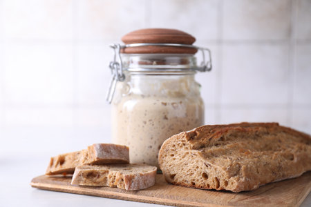 Sourdough starter in glass jar and fresh bread on light tableの写真素材