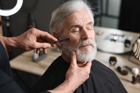 Professional barber shaving client's beard with blade in barbershopの写真素材