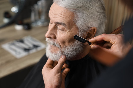 Professional barber shaving client's beard with blade in barbershop, space for textの写真素材