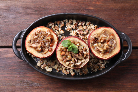 Tasty baked apples with nuts, honey and mint in baking dish on wooden table, top viewの写真素材