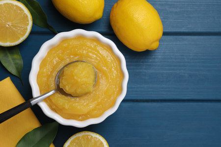 Delicious lemon curd in bowl, fresh citrus fruits and spoon on blue wooden table, flat lay. Space for textの写真素材
