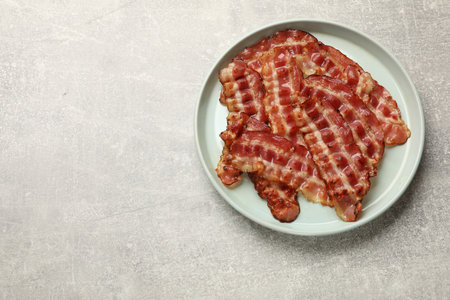 Plate with fried bacon slices on gray textured table, top view. Space for textの写真素材