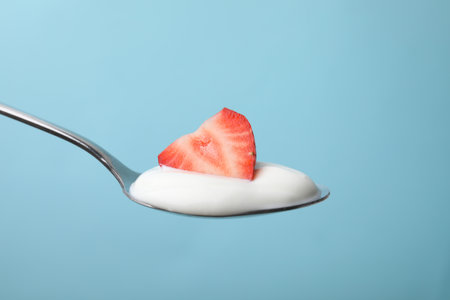 Delicious natural yogurt with fresh strawberry in spoon on light blue backgroundの写真素材