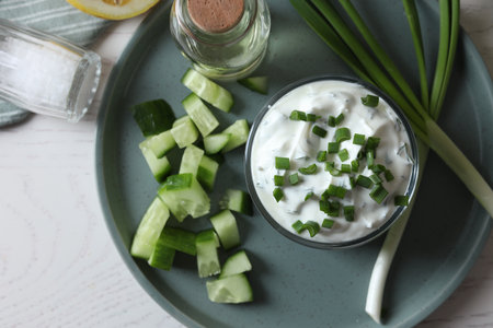 Delicious yogurt, green onion, cucumbers and spices on white wooden table, top viewの写真素材