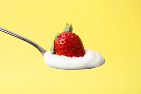 Spoon with yogurt and strawberry on yellow background, closeupの写真素材