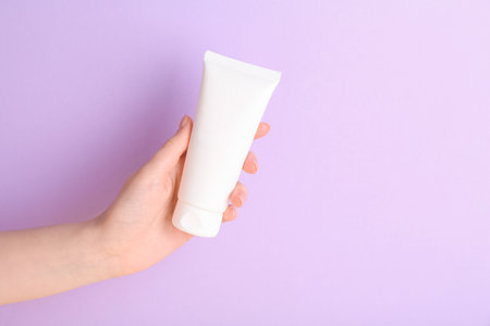 Woman with tube of cream on lilac background, closeupの写真素材
