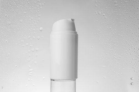 Bottle with moisturizing cream on gray background, view through wet glass