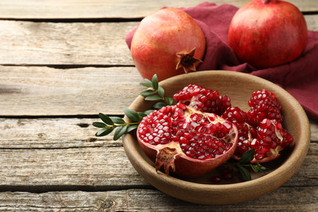Fresh pomegranates and green leaves on wooden table, space for textの写真素材