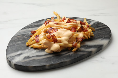 Delicious French fries with bacon and cheese sauce on white marble table, closeup