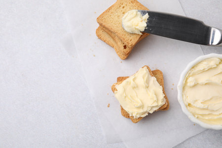 Slices of bread with tasty butter and knife on light gray table, flat lay. Space for textの写真素材