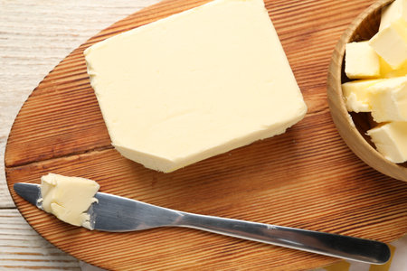 Tasty butter and knife on light wooden table, top view