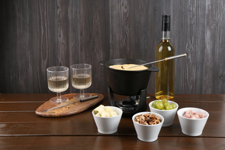 Fondue pot with tasty melted cheese, forks, wine and different snacks on wooden tableの写真素材