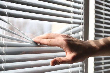 Man separating slats of white blinds indoors, closeupの写真素材