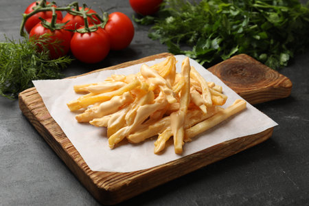 Delicious French fries with cheese sauce, tomatoes and dill on black table