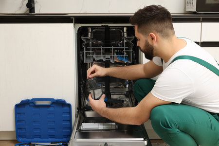 Repairman holding drain filter near dishwasher in kitchenの写真素材