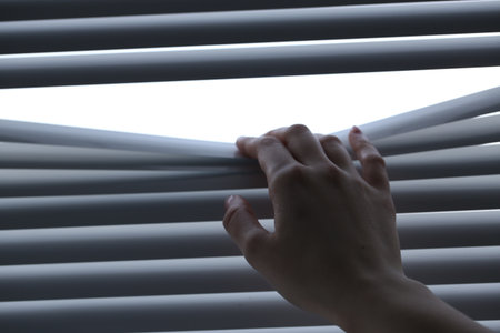 Woman separating slats of white blinds indoors, closeup