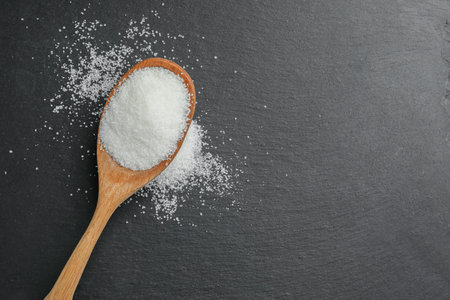 Spoon with granulated sugar on black table, top view. Space for text