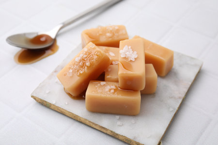 Delicious candies with sea salt and caramel sauce on white tiled table, closeupの写真素材