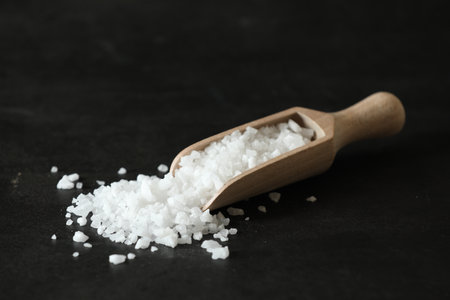 Organic salt and wooden scoop on black tableの写真素材