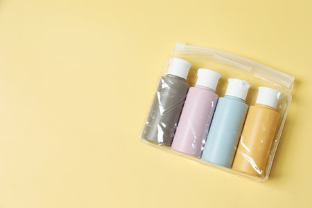 Cosmetic travel kit in plastic bag on yellow background, top view. Space for text